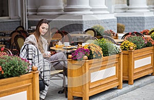 Young stylish woman having a french breakfast with coffee and cake sitting at the cafe terrace