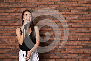 Young stylish woman posing with microphone near brick wall.