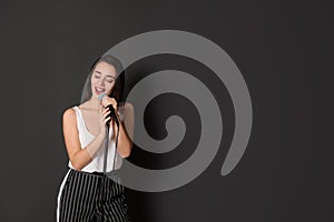 Young stylish woman singing in microphone on dark background.
