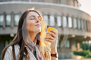 Young stylish woman in the street drinking morning coffee in sunshine light