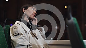 Young stylish woman wearing on wireless headphones and listening to music on mobile phone in public transport. City