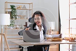 Young success american businesswoman raising her hands up and laughing with happiness at office