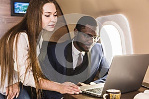 Young successful African-American businessman with glasses and an attractive female workmate blonde in a private jet