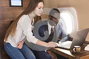 Young successful African-American businessman with glasses and an attractive female workmate blonde in a private jet