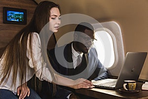 Young successful African-American businessman with glasses and an attractive female workmate blonde in a private jet