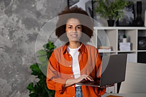 Young successful African American woman entrepreneur, ffice worker or CEO working using laptop, stands in modern office or