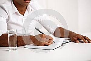 Young successful african businessman writing in notebook, sitting at workplace.