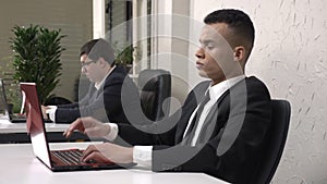 A young successful African male businessman working in the office on a laptop, tired, holding his head, a headache