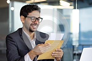 Young successful arab businessman at workplace inside office, man smiling satisfied received mail letter envelope