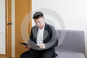 Young successful Asian man, waiting for a job interview, in the waiting room of the office center, sitting on a chair near the