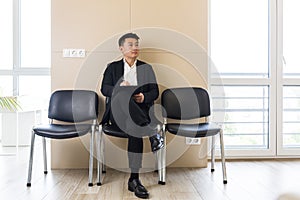 Young  Asian man, waiting for a job interview, in the waiting room of the office center, sitting on a chair near the