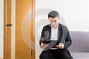 Young successful Asian man, waiting for a job interview, in the waiting room of the office center, sitting on a chair