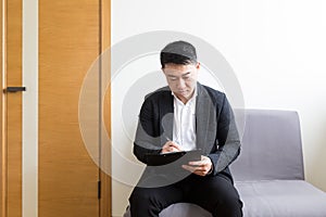 Young successful Asian man, waiting for a job interview, in the waiting room of the office center, sitting on a chair near the