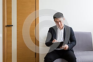 Young successful Asian man, waiting for a job interview, in the waiting room of the office center, sitting on a chair near the