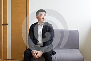 Young successful Asian man, waiting for a job interview, in the waiting room of the office center, sitting on a chair near the