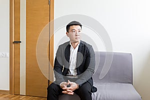 Young successful Asian man, waiting for a job interview, in the waiting room of the office center, sitting on a chair near the