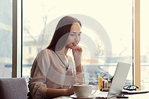 young successful attractive long-haired woman businesswoman sitting at a table in a cafe with laptop and Cup of coffee.