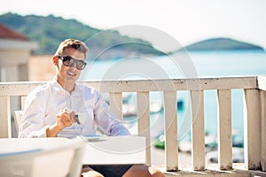 Young successful business man enjoying espresso coffee beverage in sunny marine panoramic cafe.