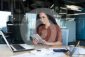 Young successful business woman working inside modern office building, Hispanic woman using tablet computer smiling and