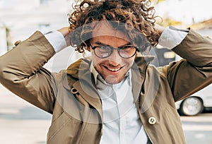 A young successful businessman in eyewear smiling broadly posing outdoors. Male entrepreneur resting in the city street. Smart guy