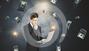 Young successful businessman with laptop and dollar bill money rain on dark wall background. Success, money and lottery winner