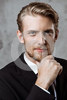 Young successful businessman posing with hand on chin over grey background.