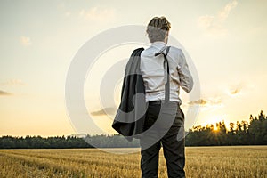 Young successful businessman standing in wheat field looking gaz