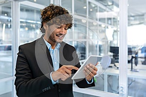 Young successful businessman with tablet computer , smiling Hispanic man working inside a modern office building at work