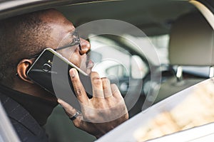 Young successful businessman talking on the phone sitting in the backseat of a expensive car. Negotiations and business
