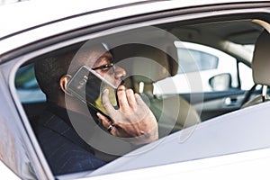 Young successful businessman talking on the phone sitting in the backseat of a expensive car. Negotiations and business