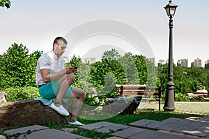 Young successful businessman in a white shirt. A man is sitting on the grass, working on a smartphone in a city park on a green