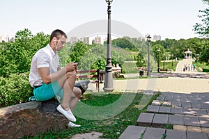 Young successful businessman in a white shirt. A man is sitting on the grass, working on a smartphone in a city park on a green
