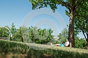 Young successful businessman in a white shirt. A man is sitting on the grass, working on a smartphone in a city park on a green