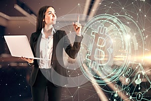 Young successful businesswoman with laptop stands on the Bitcoin symbol background