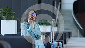 Young successful businesswoman talking on phone and sitting in airport before business trip spbi.