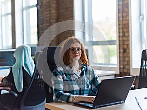 A young and successful businesswoman with vibrant orange hair engages in focused work within a modern office, showcasing photo