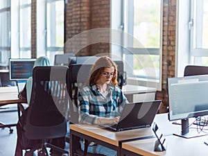 A young and successful businesswoman with vibrant orange hair engages in focused work within a modern office, showcasing photo