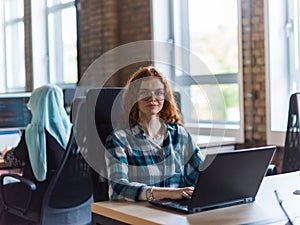 A young and successful businesswoman with vibrant orange hair engages in focused work within a modern office, showcasing photo