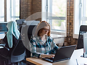 A young and successful businesswoman with vibrant orange hair engages in focused work within a modern office, showcasing photo