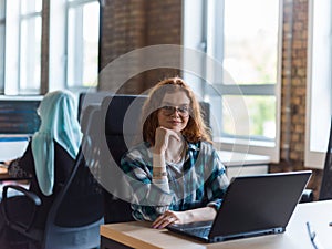 A young and successful businesswoman with vibrant orange hair engages in focused work within a modern office, showcasing photo