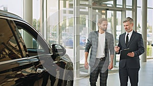 Young successful customer man deciding to buy new auto in showroom. Happy car salesman and male customer in auto