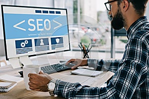 young successful developer sitting at workplace with SEO sign