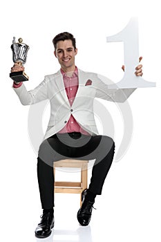 Young successful elgant businessman holding trophy and number one up