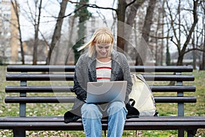 Young successful hipster businesswoman generation Z sitting on park bench working on laptop computer. Professional business female