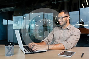 Young successful Indian programmer working inside modern development company, man using laptop to write code for