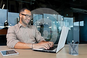 Young successful Indian programmer working inside modern development company, man using laptop to write code for