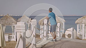 A young successful man is enjoying his vacation at a luxurious seaside resort. He strolls along the beach, savoring the