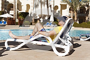 Young and successful man lying on a sun lounger at the hotel near sweeming pool. Relax in summer pool. Concept time to