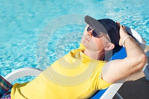 Young and successful man lying on a sun lounger at the hotel near sweeming pool. Relax in summer pool. Concept time to