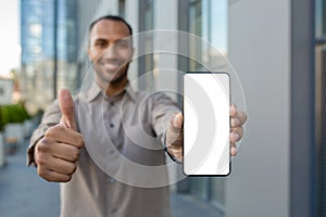Young successful man showing white phone screen to camera, businessman recommending app, looking happily at camera
